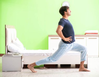 Pijamalı genç adam sabah egzersizi yapıyor.