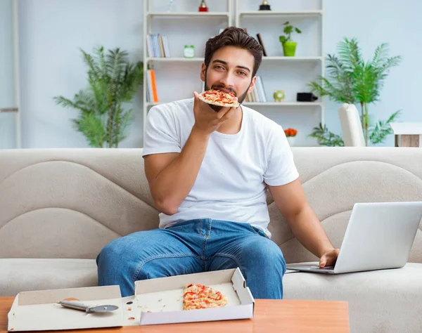 Pizza yiyen adam evde yemek yiyor, dinleniyor.