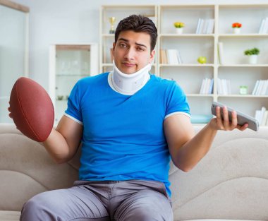 Boynu yaralanmış bir adam evde Amerikan futbolu seyrediyor.