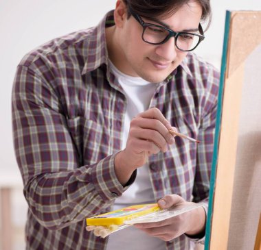 Genç erkek sanatçı parlak stüdyoda resimler çiziyor.