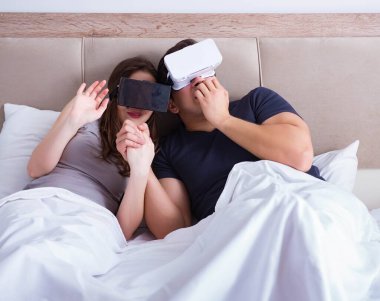 Yatakta sanal gerçeklik gözlüklü eş ve koca.