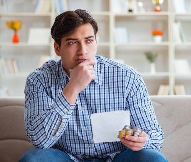 Kanepede ilaç ve reçeteyle oturan genç adam.