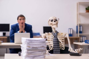 Ofiste iskeletleri olan genç bir erkek çalışan.