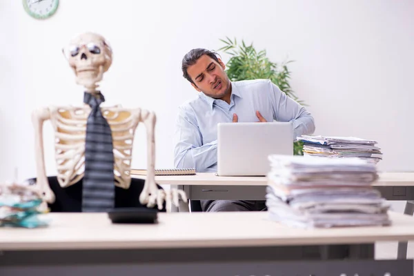 Ung manlig anställd och skelett på kontoret — Stockfoto