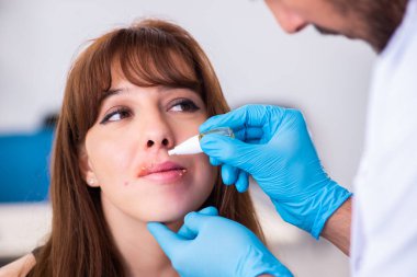 Genç bir kadın erkek doktor dermatoloğunu ziyaret ediyor.