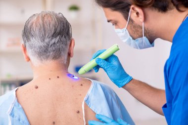 Yaşlı adam genç erkek doktor dermatoloğu ziyaret ediyor.