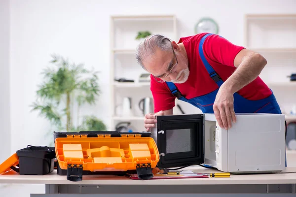 Old male contractor repairing microwave indoors — Stock Photo, Image