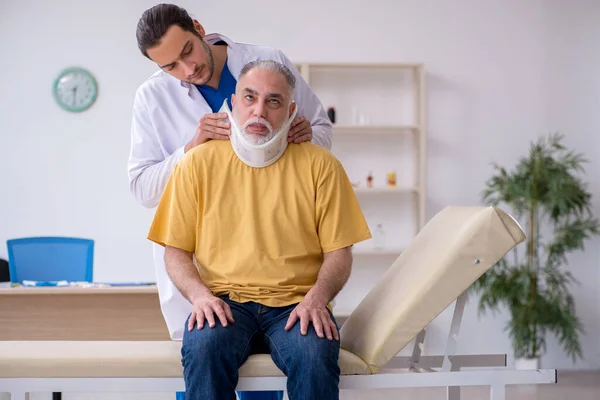 Yaşlı boynu yaralı bir adam genç erkek doktoru ziyaret ediyor. — Stok fotoğraf