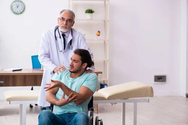 Ervaren arts en jonge mannelijke patiënt in rolstoel — Stockfoto