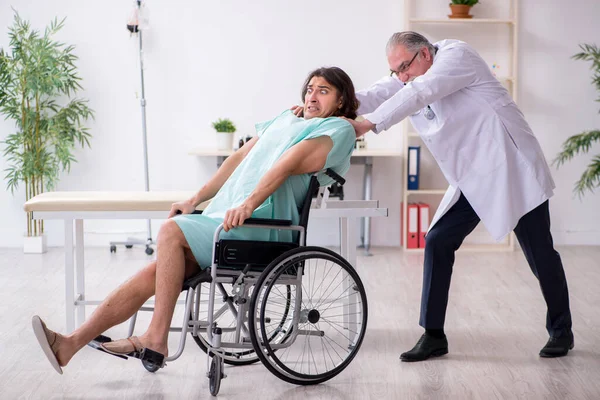 Jovem paciente do sexo masculino em cadeira de rodas e médico traumatologista experiente — Fotografia de Stock