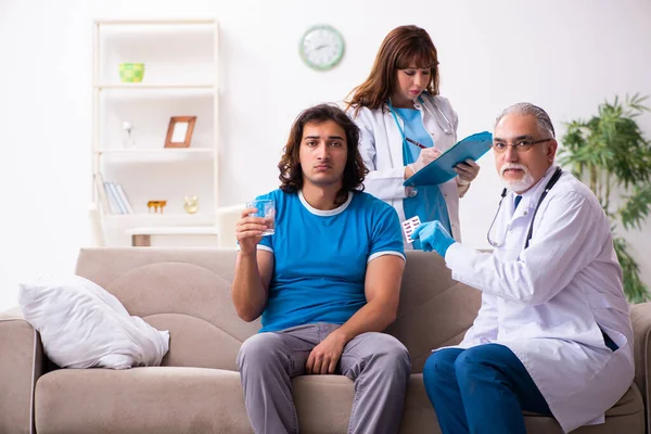 Zwei Ärzte besuchen kranken jungen Mann zu Hause — Stockfoto