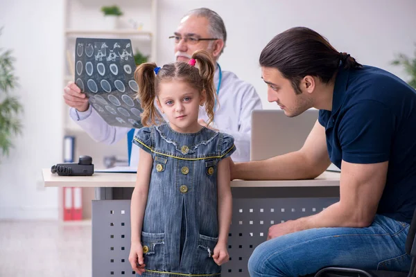 Young father and his daughter visiting old male doctor