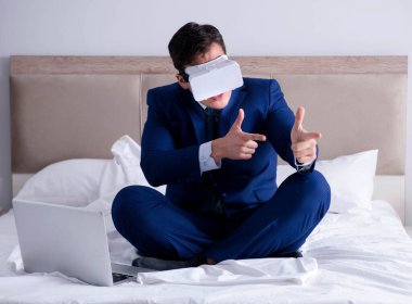 Yatak odasında sanal gerçeklik kulaklığı takan bir iş adamı.