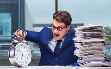 Yığınla evrak işi ve alarm sistemi olan bir iş adamı.
