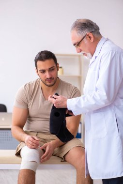 Deneyimli doktor travmatolog genç erkek hastayı muayene ediyor.