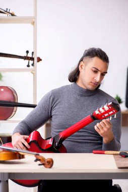 Gitarı tamir eden genç bir erkek tamirci.