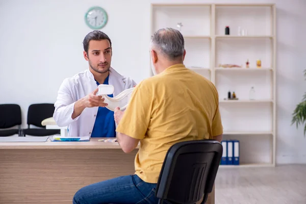 Velho pescoço ferido homem visitando jovem médico masculino — Fotografia de Stock