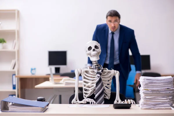 Young male employee with skeletons in the office — Stock Photo, Image