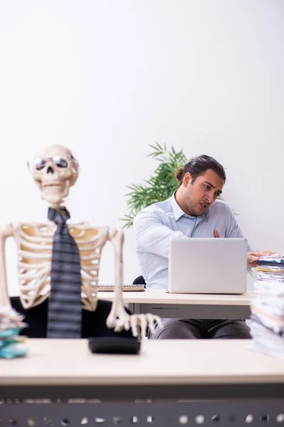 Young male employee and skeleton in the office — Stock Photo, Image