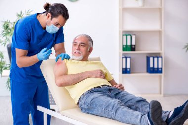 Yaralı yaşlı adam genç erkek doktor travmatoloğu ziyaret ediyor.