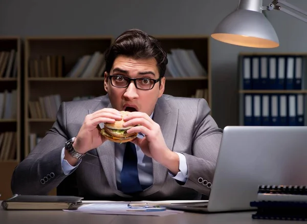 Affärsman sent på kvällen äter en hamburgare — Stockfoto