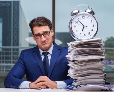 Yığınla evrak işi ve alarm sistemi olan bir iş adamı.