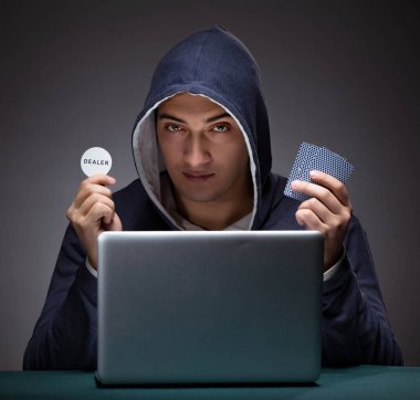 Kapüşonlu genç adam dizüstü bilgisayarın önünde oturuyor.