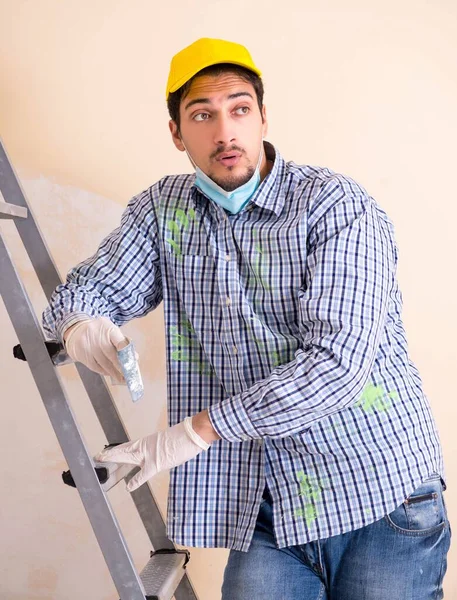 Genç müteahhit zımpara kağıdıyla duvarı zımparalıyor.