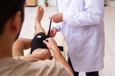 Deneyimli doktor travmatolog genç erkek hastayı muayene ediyor.