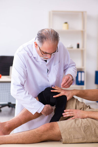 Опытный врач-травматолог, осматривающий молодого пациента