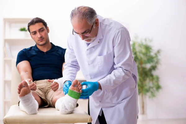 Young injured man visiting old doctor traumatologist — Stock Photo, Image