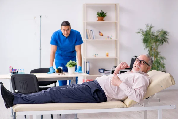 Vecchio paziente visita giovane medico maschio per la terapia endovenosa — Foto Stock