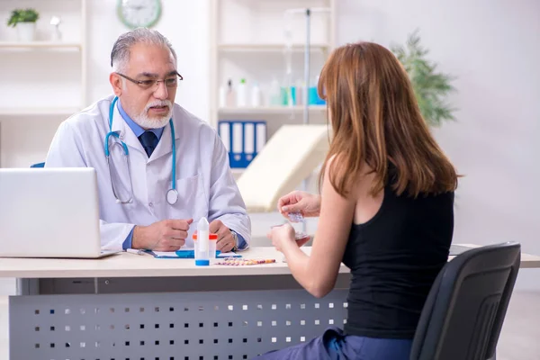 Mujer joven visitando viejo médico masculino — Foto de Stock