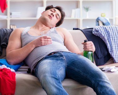 Dağınık bir odada alkol alan genç bir öğrenci.