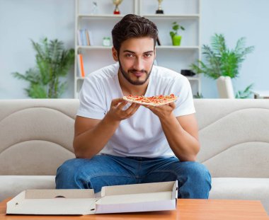 Pizza yiyen adam evde yemek yiyor, dinleniyor.