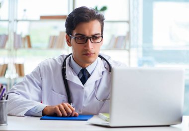 Hastane kliniğinde masasında oturan genç bir erkek doktor.