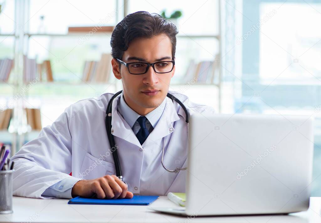 Young male doctor sitting at desk in hospital clinic