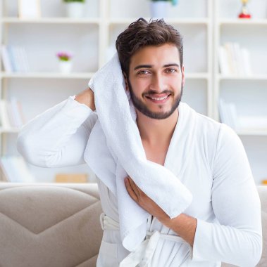 Duş aldıktan sonra bornozlu genç adam saçlarını bir towe ile kurutuyor.