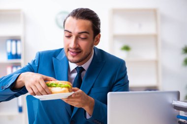 Genç erkek çalışan işyerinde kahvaltı yapıyor.