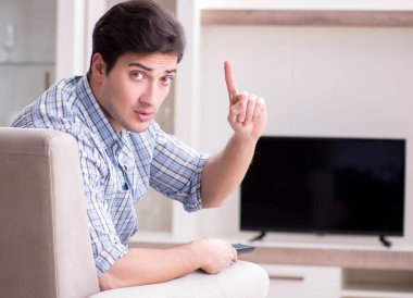 Genç adam evde televizyon izliyor.