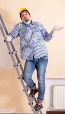 Genç müteahhit zımpara kağıdıyla duvarı zımparalıyor.