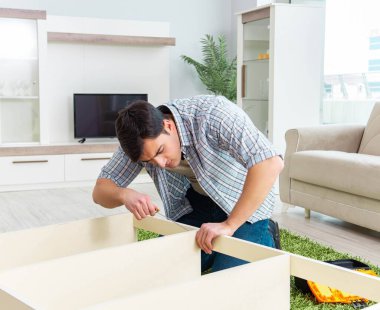 Adam evde mobilya montajı yapıyor.