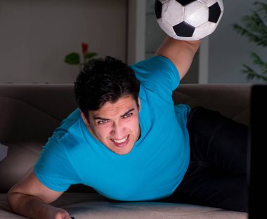 Genç adam gece geç saatlerde futbol seyrediyor.