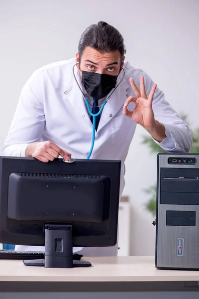 Joven doctor masculino con estetoscopio reparando computadora —  Fotos de Stock