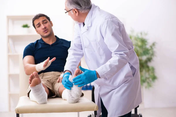 Jonge gewonde man bezoekt oude dokter traumatoloog — Stockfoto