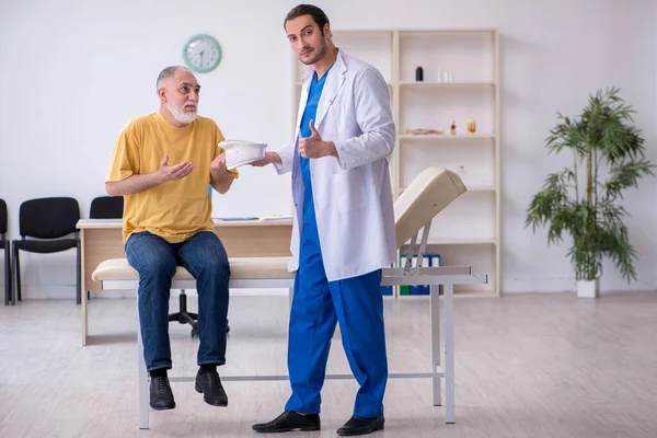 Yaşlı boynu yaralı bir adam genç erkek doktoru ziyaret ediyor. — Stok fotoğraf
