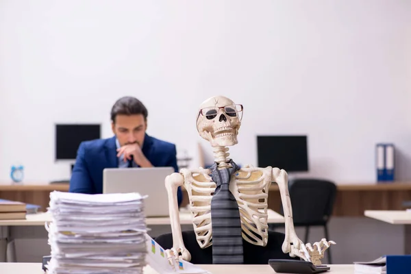 Young male employee with skeletons in the office — Stock Photo, Image