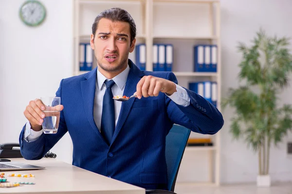 Young male employee and a lot of pills on the desk — Stock Photo, Image