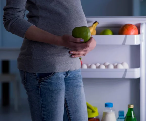 Mulher grávida perto de geladeira à procura de alimentos e lanches à noite — Fotografia de Stock