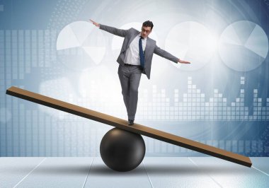 Top ve tahterevalli üzerinde denge kurmaya çalışan bir işadamı